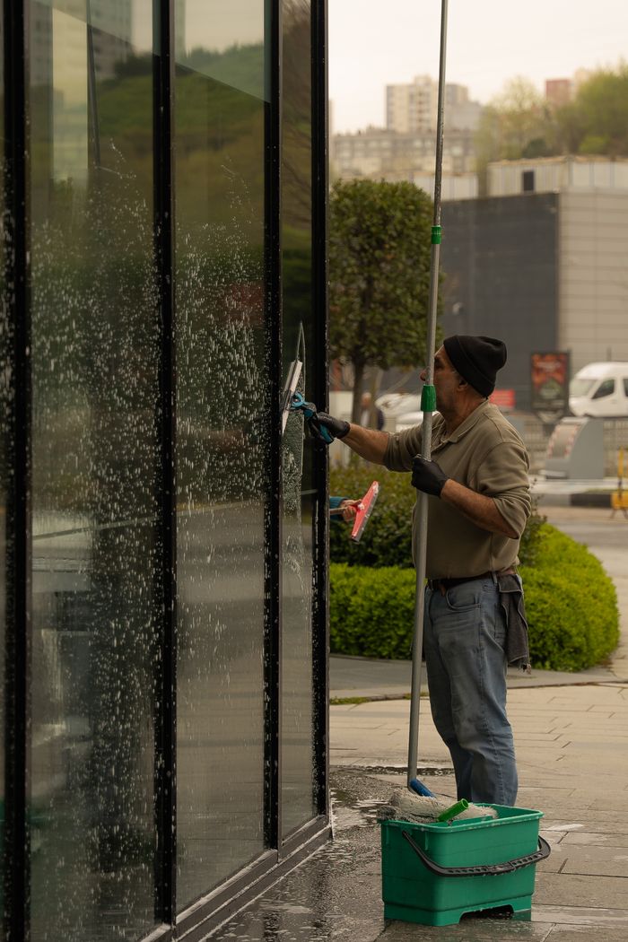 A window cleaner using a squeegee to clean a glass building facade on a cloudy day.